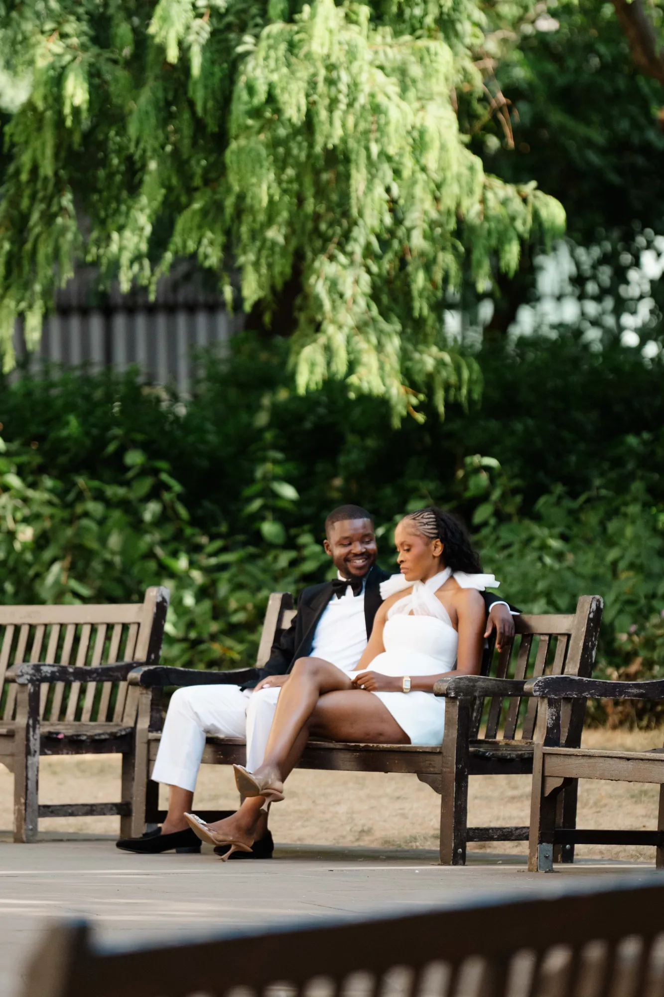 Kennedy and Didimalang sitting close together on a park bench beneath a willow tree